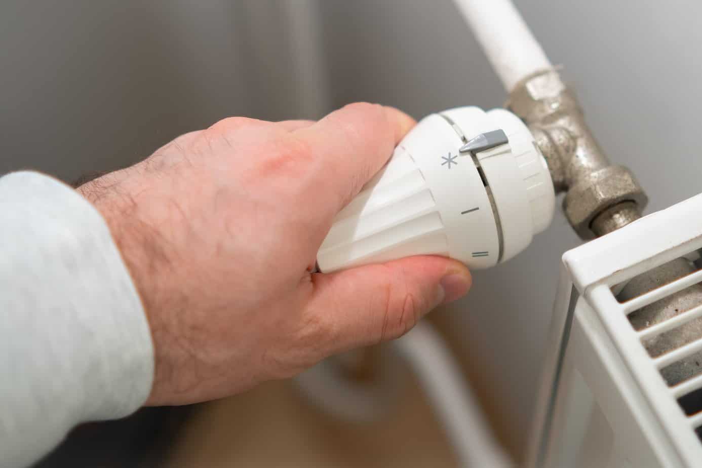 Man hand regulates temperature knob of heating radiator to reduce heating costs.