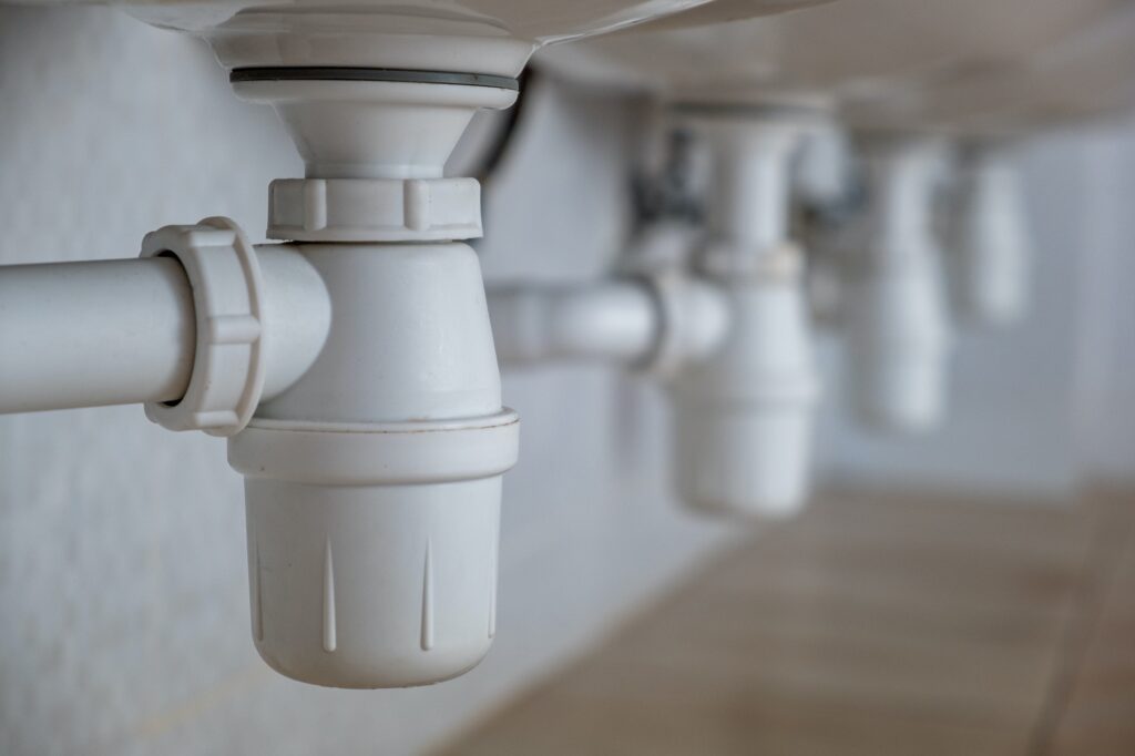 Close up of white plastic pipe drain under washing sink in bathroom.