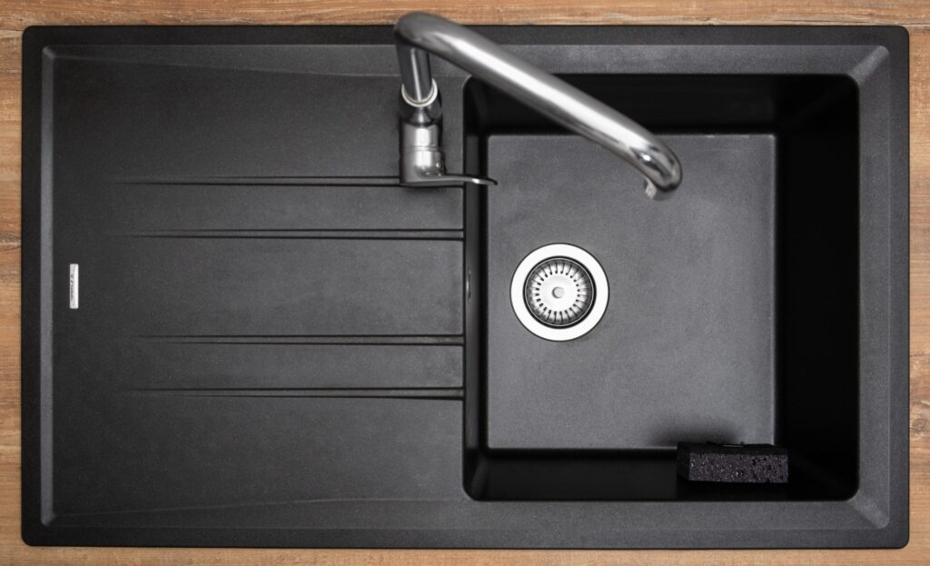 Organizer holder for a kitchen sponge in a black granite sink. Storage and organization of space